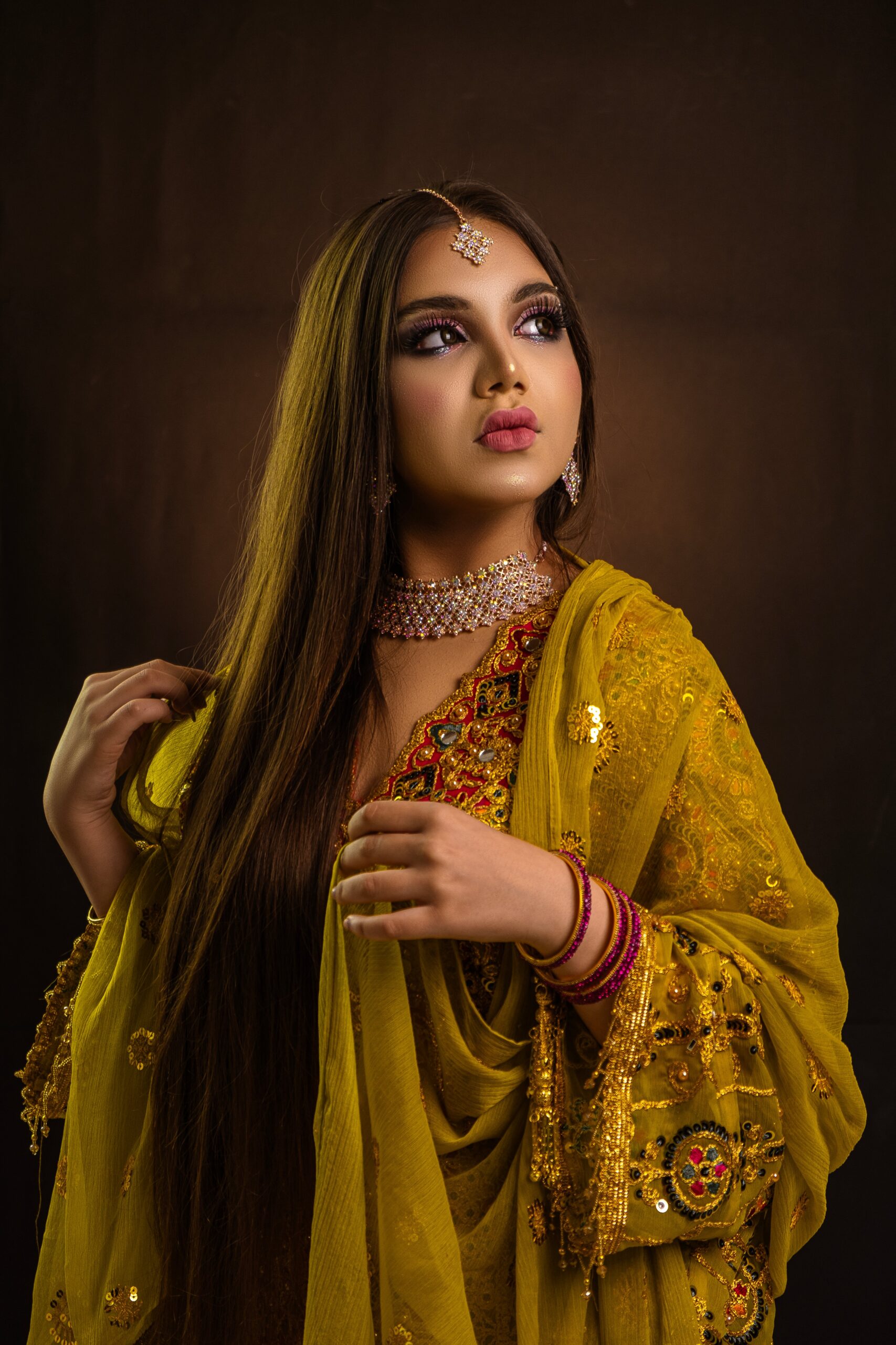 Stylish portrait of a woman wearing a yellow sari, showcasing intricate jewelry and traditional fashion.